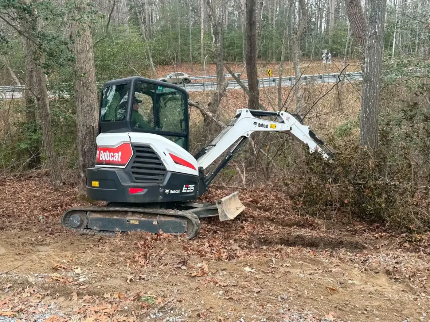Mini excavator pulling brush at the edge of a wooded lot